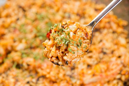 Spoon scooping up stir-fried kimchi rice with kimchi, carrots and onions, made on iron plateの写真素材