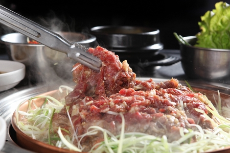 Pincers picking up marinated bulgogi with seasoned green onions, on iron plateの写真素材