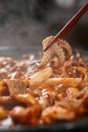 Stir-fried webfoot octopus and pork belly being grilled on pan, with chopsticksの写真素材