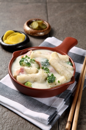 Carbonara spicy rice cake with broccoli and bacon inside served in bowl with chopstickの写真素材