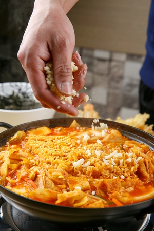 Hand that is putting cheese on Spicy Rice Cake with ramen noodles on pan on burner