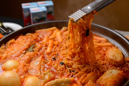 Spicy Rice Cake with Ramen Noodles with Egg and Dumplings served on pan with tongs