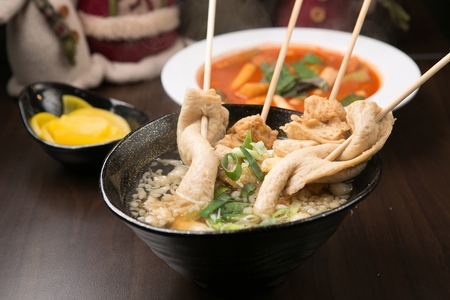 Fish Cake Soup with spring onion and fried tofu inside with spicy rice cake and pickled radish served in bowlの写真素材
