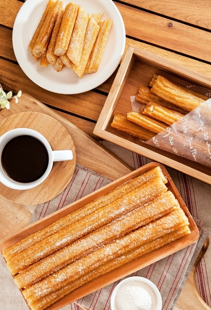 Churros with sprinkled sugar on top served on wooden plate with coffeeの写真素材