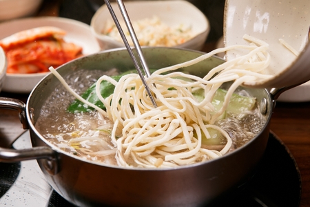 Chopped noodle soup broth and vegetables inside pot and chopsticks putting in chopped noodles inside the potの写真素材
