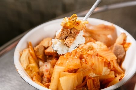 Kimchi stew with pork inside served in bowl and spoon holding riceの写真素材