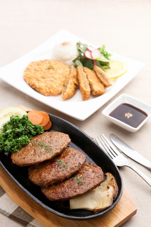 Grilled short rib patties with mushrooms, carrots, parsley, and lemon served on iron plateの写真素材