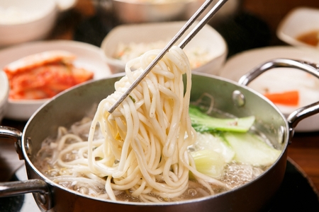 Chopsticks grabbing chopped noodle from chopped noodle soup with chinese cabbage served in potの写真素材