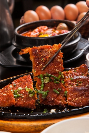 Chopsticks grabbing Marinated Grilled Pollack with chives and sesame seeds on top served on iron plateの写真素材