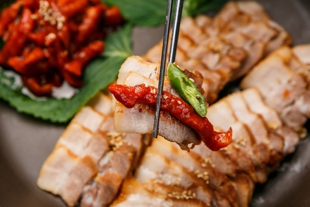 chopsticks holding Korean cuisine Suyuk, boiled pork, spicy dried radish and green pepper from porcelain bowlの写真素材