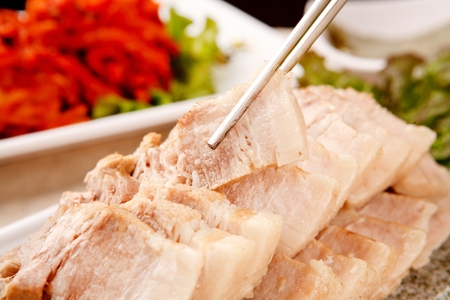 chopsticks holding Korean cuisine Suyuk, boiled pork slices from plateの写真素材