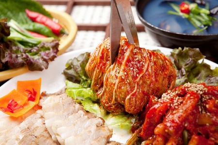scissors cutting cabbage kimchi with sesame seeds, boiled pork slices on plateの写真素材