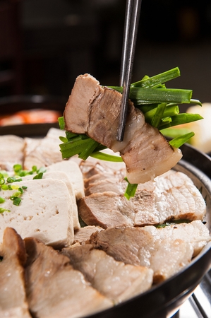 Korean cuisine Suyuk, boiled pork held in chopsticks from fry pan, tofu and side dishの写真素材