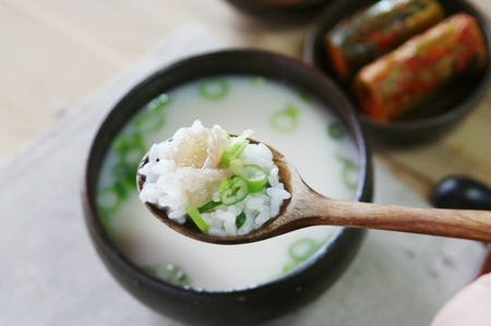 Korean cuisine ox knee soup with spring onions served in Ttukbaegi, earthen pot, spoon scooping soup...