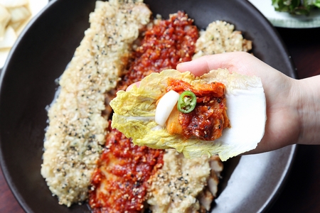 Hands making cabbage wrap with Korean cuisine Suyuk, boiled pork with chopped galirc sauce from fry...