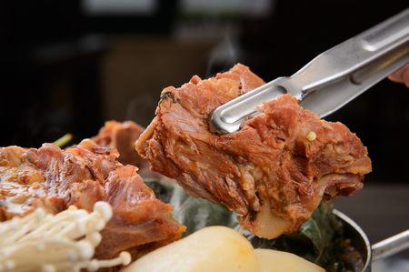 Korean cuisine Gamjatang, spicy pork back-bone stew with pork held in tongs