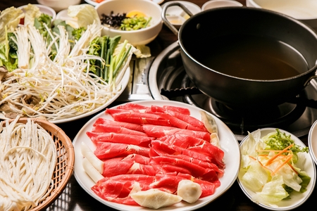 Shabu-shabu restaurant setting, beef and vegetable platters, hot pot and side dishの写真素材