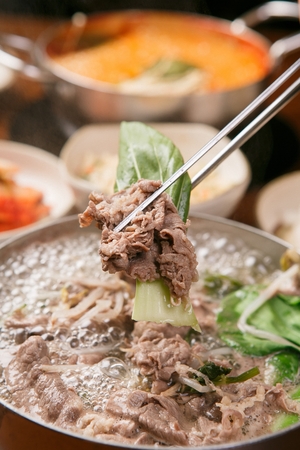 chopsticks holding beef from Shabu-shabu hot pot with bean sprouts, bok choy and vegetables in potの写真素材