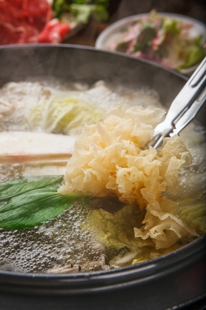 tongs putting mushrooms into Shabu-shabu hotpot with mushroom, chives and bok choy in potの写真素材