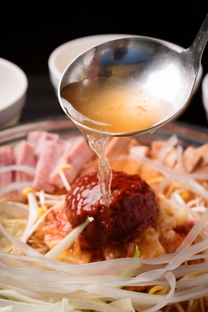 Ladle pouring soup to Budae jjigae, spicy sausage stew with ham, noodles, fish cake and bean sprouts in fry panの写真素材