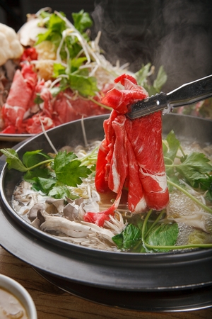 tongs putting beef into Shabu-shabu hotpot with mushroom, chives and bok choy in potの写真素材