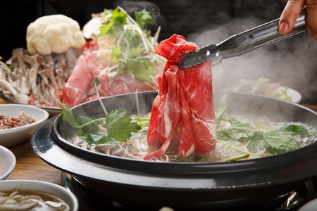 tongs putting beef into Shabu-shabu hotpot with mushroom, chives and bok choy in potの写真素材