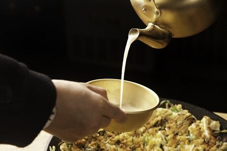 cooking Seafood Jeon, Korean pancake with green chili and greens on fry pan and hand  pouring Makgeolli, rice wineの写真素材