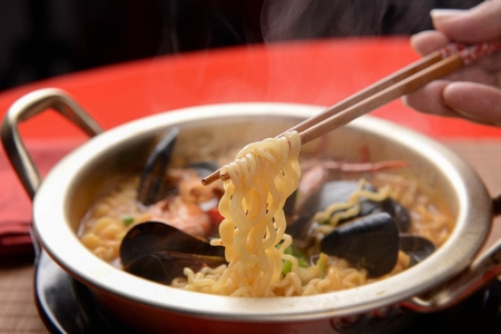 chopsticks holding noodles from Haemul Ramyeon, Korean spicy seafood noodles with spring onions and...