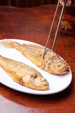 chopsticks holding grilled croaker fish from plate