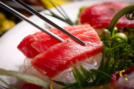 chopsticks holding tuna sashimi from plate