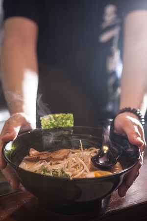 hands serving hot Japanese miso ramen bowl with soup spoonの写真素材