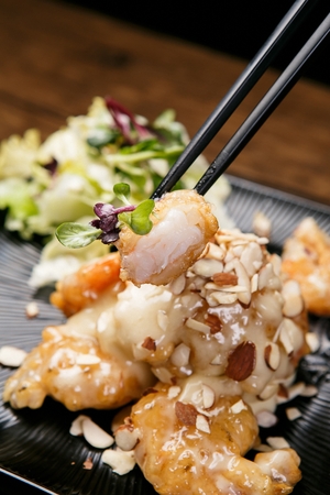 deep-fried shrimp with cream sauce and almonds, served with salad held with chopsticksの写真素材