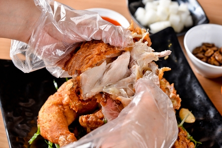 whole fried chicken with garlic being cut with handsの写真素材