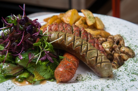 grilled sausages with small cuts on surface served with french fries and stir-fried mushroomsの写真素材