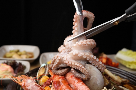 tongs holding small octopus from assorted steamed seafood in Ttukbaegi, earthen potの写真素材