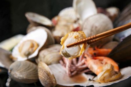 chopsticks holding clam from Jogae Jjim, steamed clams with vegetablesの写真素材