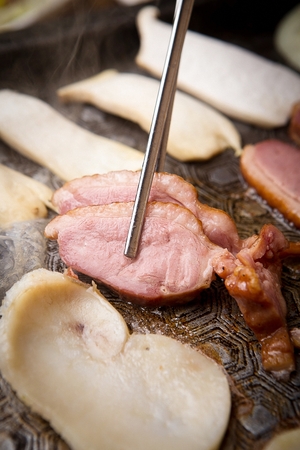 smoked duck grilled on pan held with chopsticksの写真素材