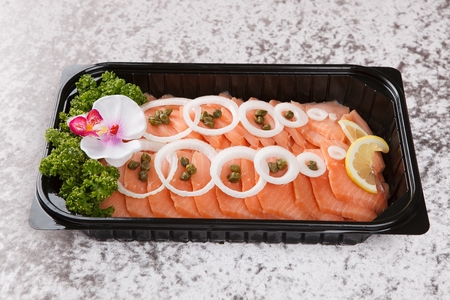 Salmon salad with sliced onions and caper, on black palstic plateの写真素材