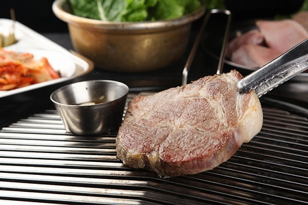 Pincers grabbing pork neck being grilled on grillの写真素材