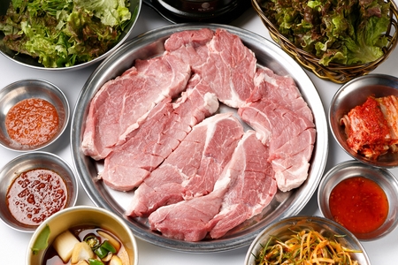 Raw pork neck with sprinkled salt on stainless plate, with side dishes, on white tableの写真素材