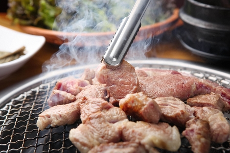 Pincers picking up pork neck being grilled on grillの写真素材
