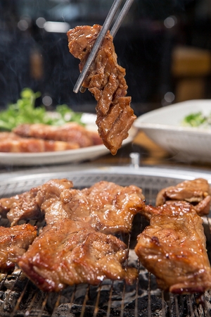 Chopsticks grabbing grilled marinated pork spareribs from grillの写真素材