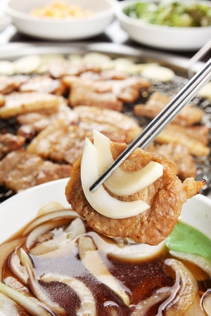 Chopsticks grabbing grilled marinated pork spareribs with seasoned onions from plateの写真素材