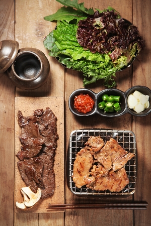 Grilled marinated pork spareribs on wooden cutting board, and marinated pork spareribs and various ingredients being grilled on grillの写真素材