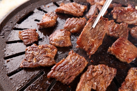 Chopsticks grabbing marinated pork spareribs being grilled on stone plateの写真素材