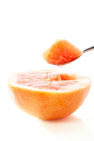 spoon scooping halved grapefruit, white backgroundの写真素材
