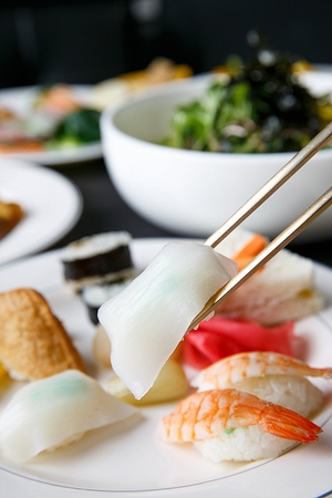 Chopsticks grabbing dried cuttlefish sushi among various kinds of sushi on white platesの写真素材