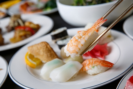 Chopsticks grabbing shrimp sushi among various kinds of sushi on white platesの写真素材
