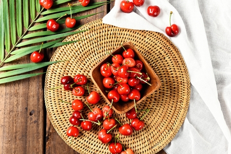 cherries on wood bowl above woven plateの写真素材