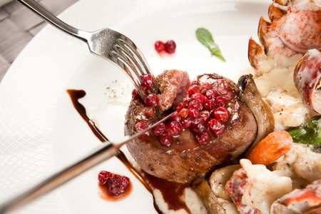 fork grabbing beef tenderloin steak and crawfish from white plateの写真素材